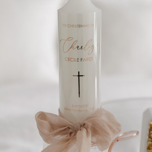 Elegant personalised Christening candle with a gold script name, cross design, and baptism date, adorned with a soft bow – perfect for a baptism keepsake.
