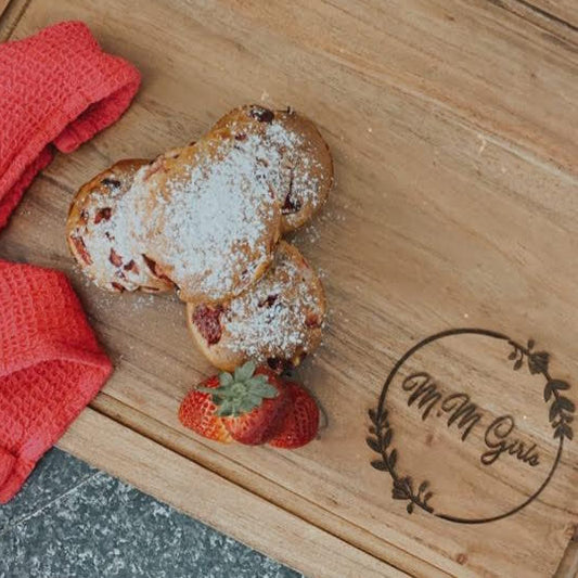 Personalised wooden serving board engraved with custom text, styled with strawberry baked goods and fresh strawberries on a dark stone surface.