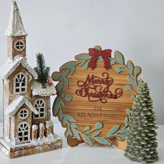 Christmas plaque with red “Merry Christmas” text, wreath design, and personalised family name, styled with festive decorations.