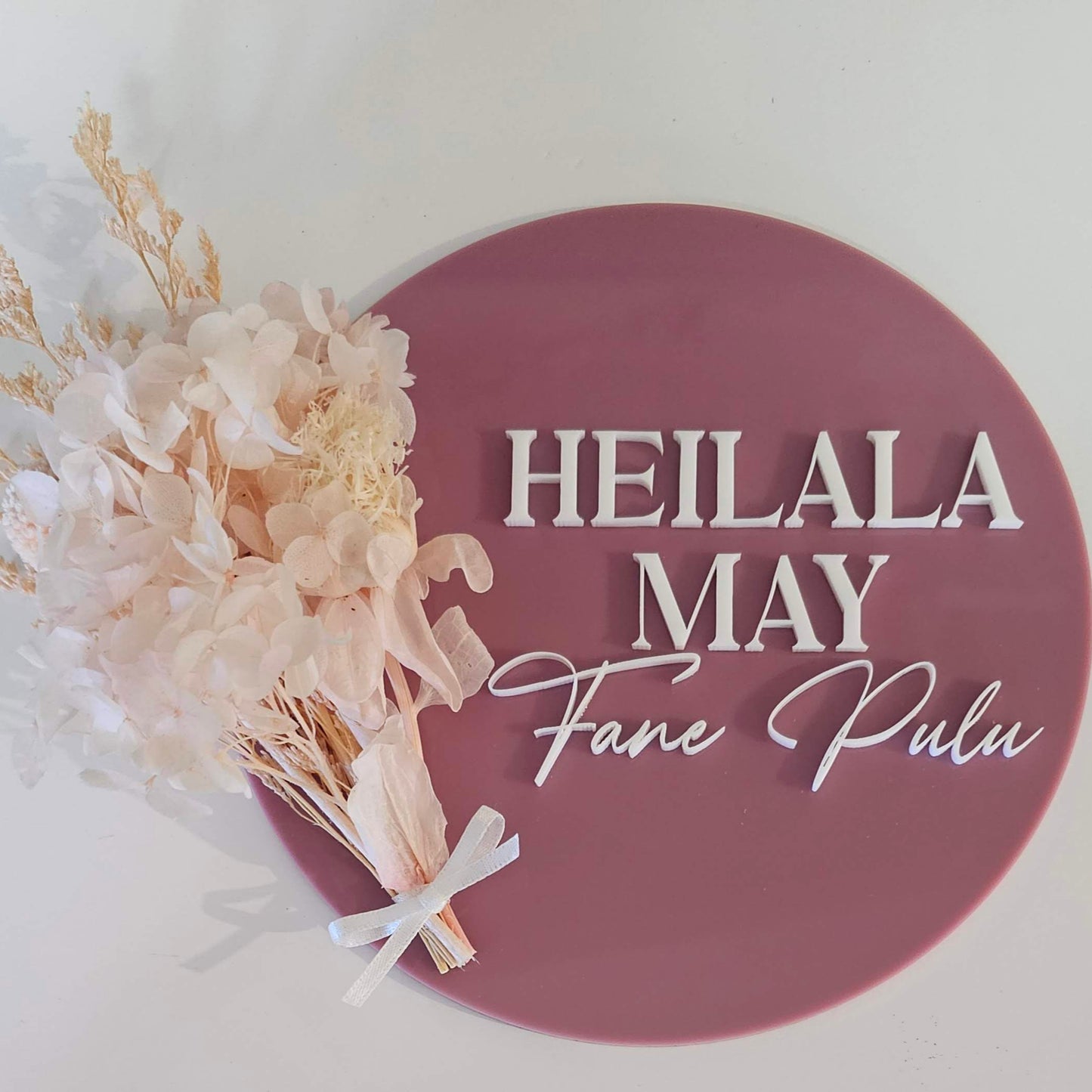 Acrylic name plaque with mauve background, white text in mixed fonts, and dried flower bundle tied with white ribbon