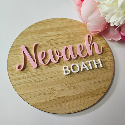 Round timber baby name plaque with raised pink cursive name and engraved white uppercase surname.