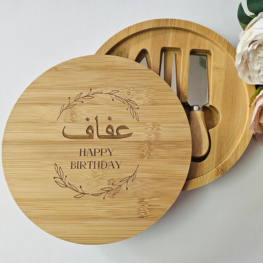 Round wooden gift box engraved with floral wreath and personalised message, containing three wooden-handled cheese knives.