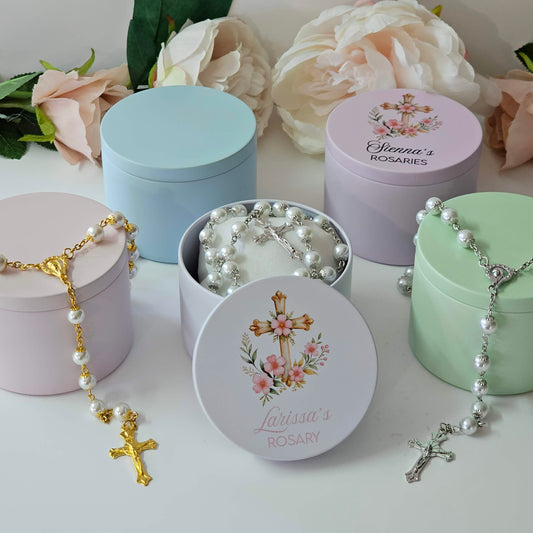 Pastel acrylic rosary containers in pink, blue, green, and lavender with personalised names and white rosaries.