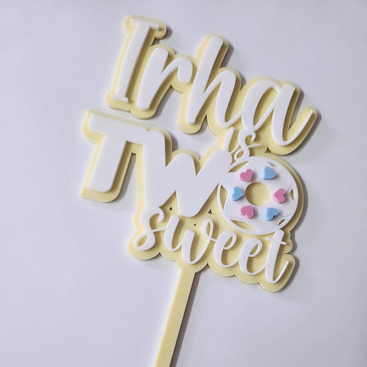 Custom "Irha is Two Sweet" cake topper with pastel yellow and white lettering, featuring a cute donut design with heart sprinkles for a 2nd birthday party.