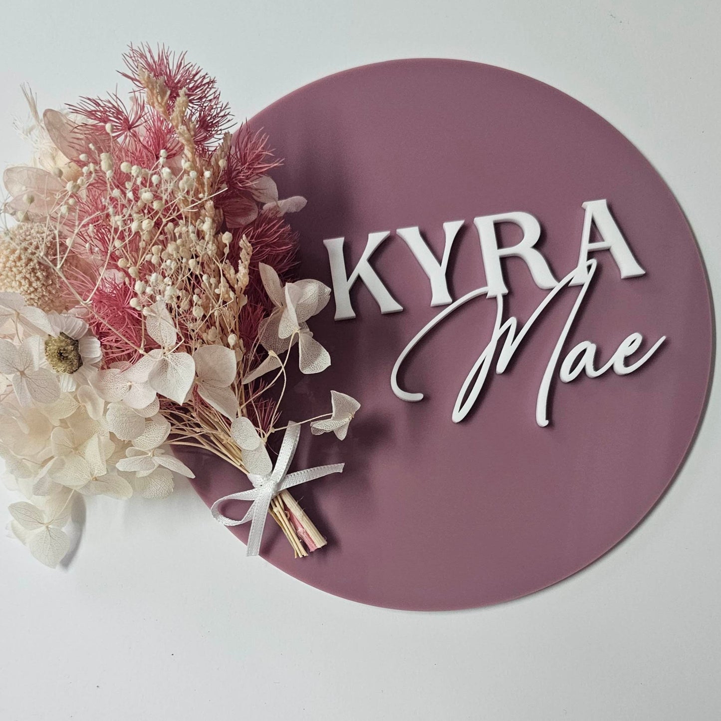 Mauve acrylic baby name sign with 3D white lettering “Kyra Mae,” styled with pink and cream dried florals