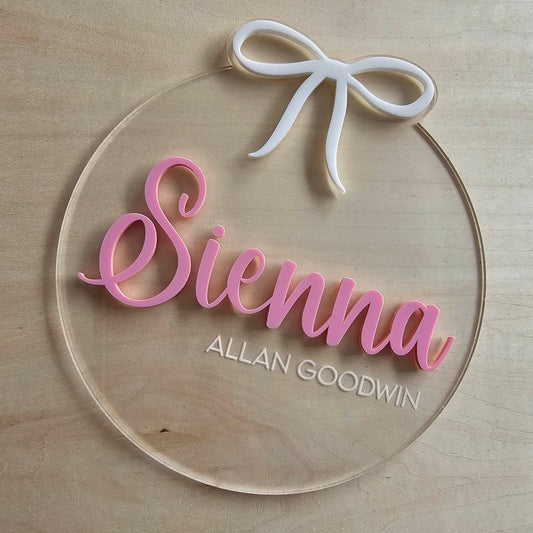 Personalised clear acrylic baby name plaque with pink 3D name, white bow, and engraved details – 15cm round