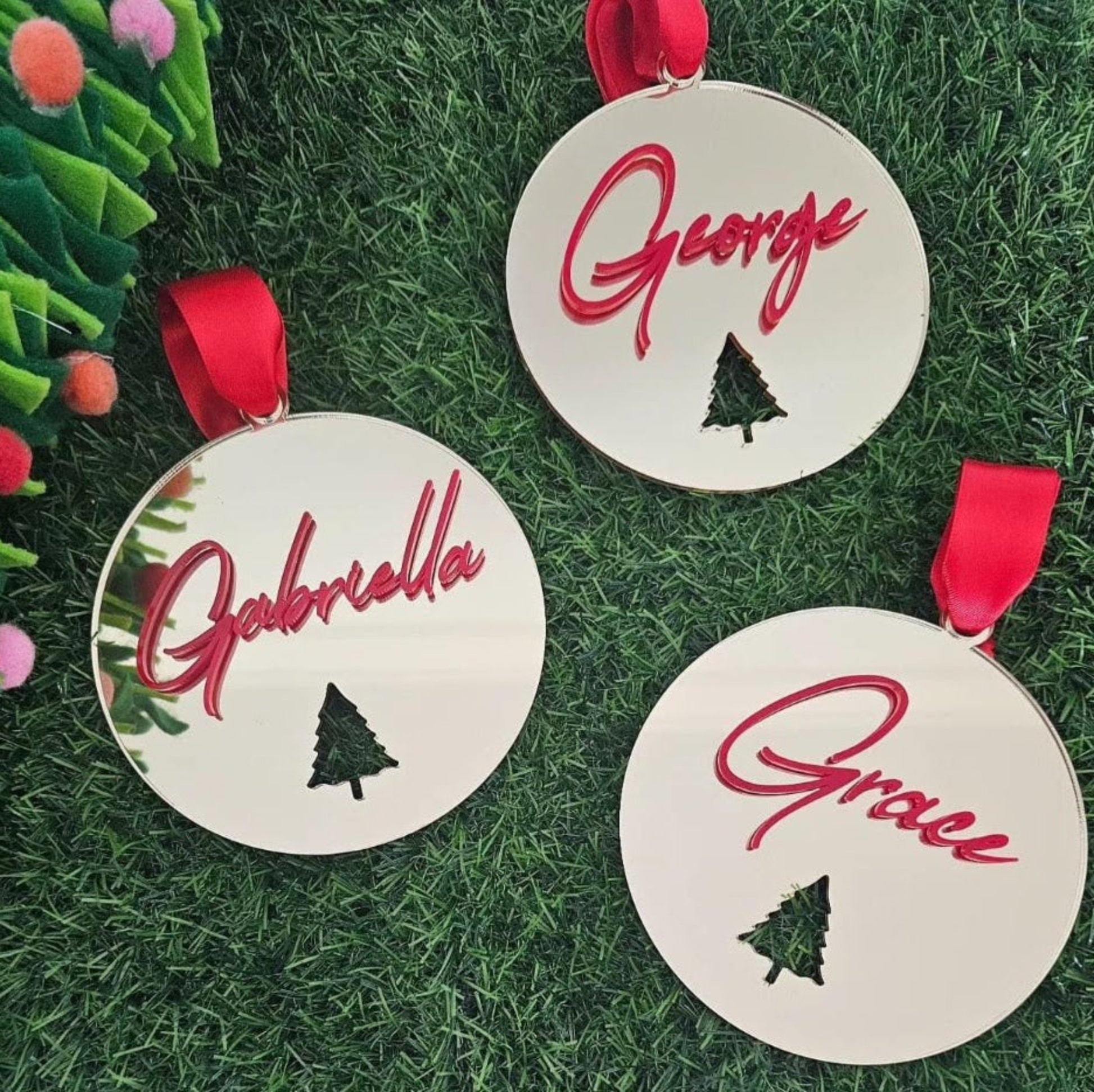 Personalised mirror acrylic Christmas baubles with red acrylic names and Christmas tree cutout — handmade festive ornaments with red ribbon